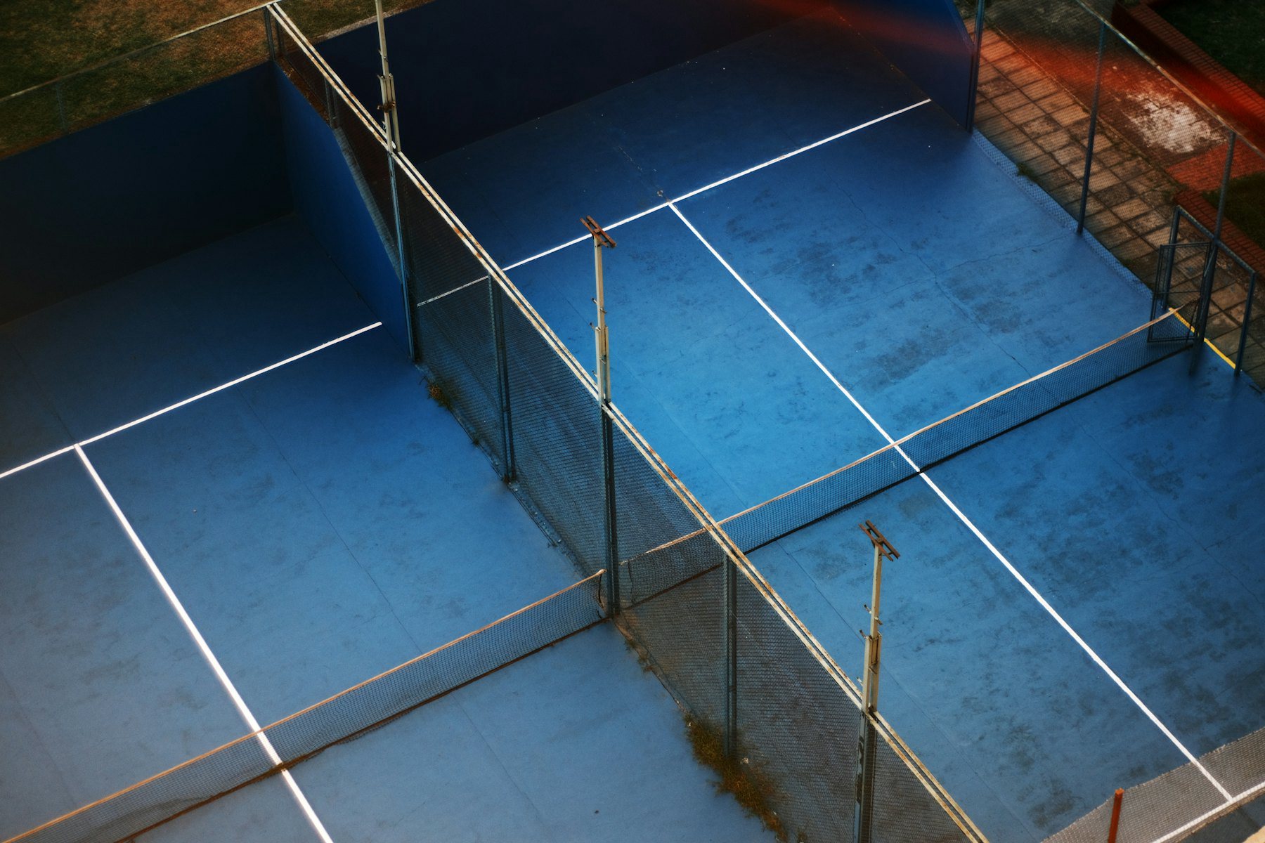 Padel courts seen from above, blue artificial grass inside glass walls and a fence