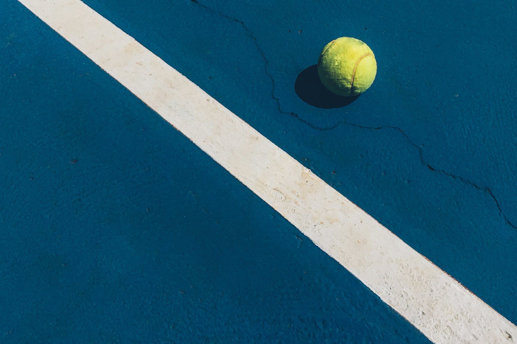 Mavi bir kortta beyaz bir çizginin yanında duran sarı bir padel topu